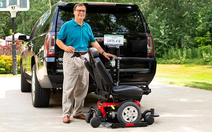 a man standing next to a scooter lift behind a suv