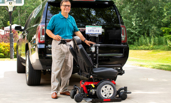 man standing next to a scooter lift on the back of a suv