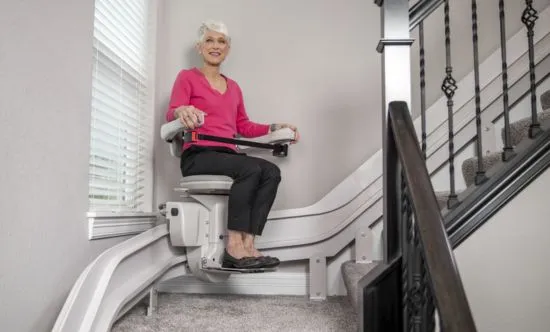 an elderly women riding a curved indoor stair lift