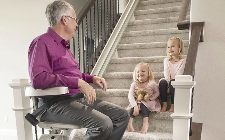 a man riding an indoor stair lift with kids sitting on the steps watching