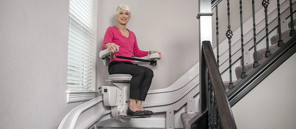 an elderly women riding a curved indoor stair lift
