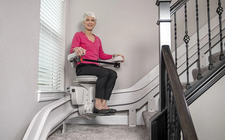 an elderly women riding a curved indoor stair lift