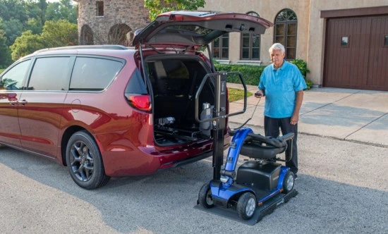 a man standing next to a scooter loaded onto a scooter lift at the back of a red van
